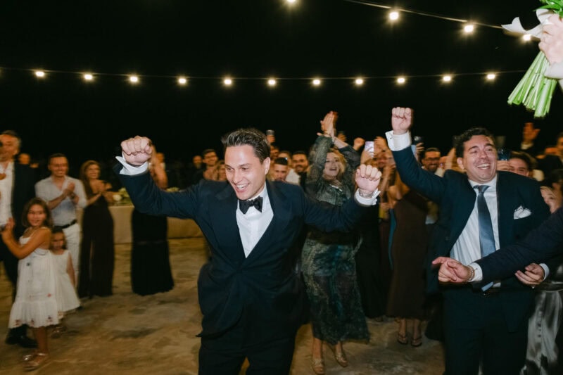 Groom dancing and celebrating at messinian wedding event at night.