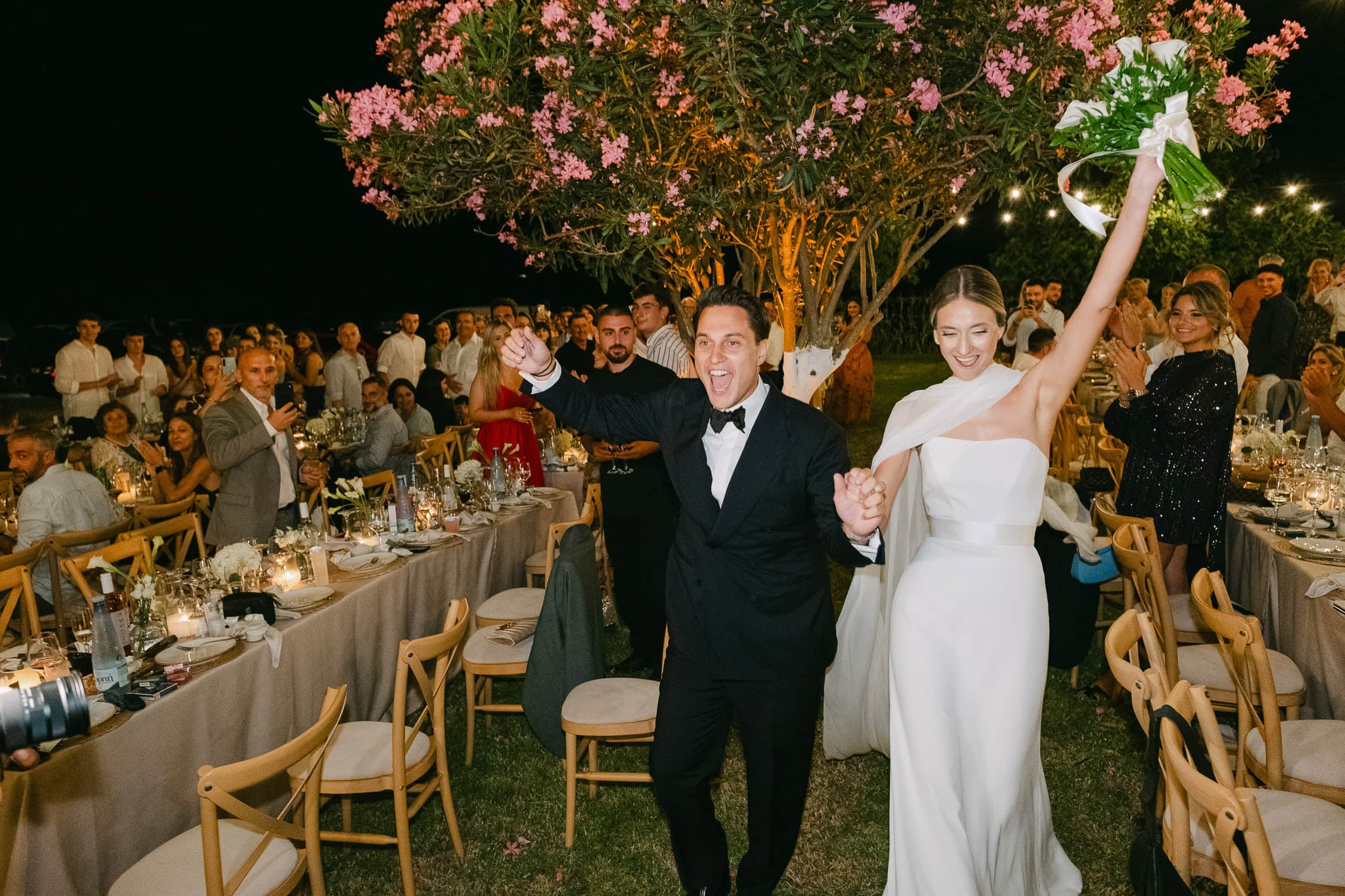 Happy bride and groom dancing at outdoor wedding reception at night.