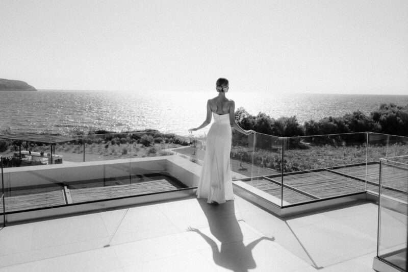 Bride in a white dress standing on a balcony with sea view.