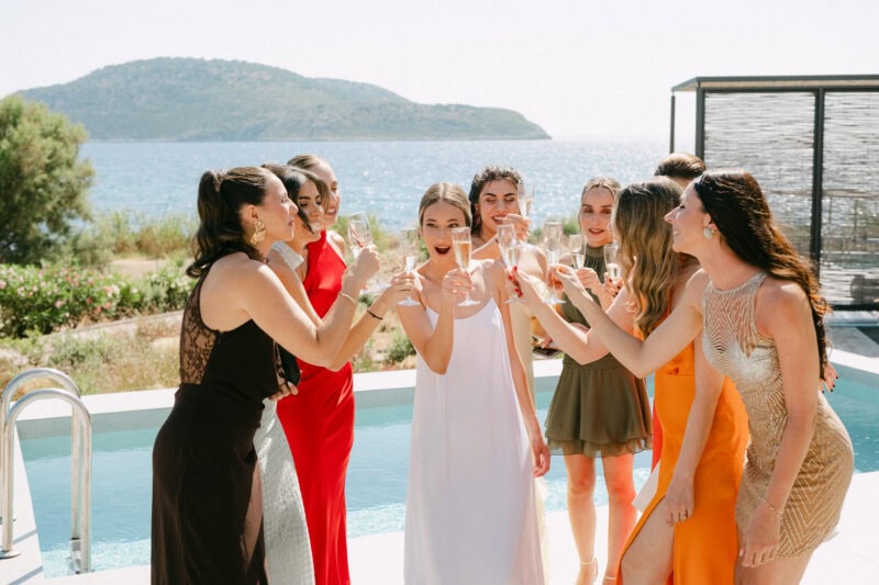 Bride and bridemaids in colorful dresses enjoying drinks by the poolside.
