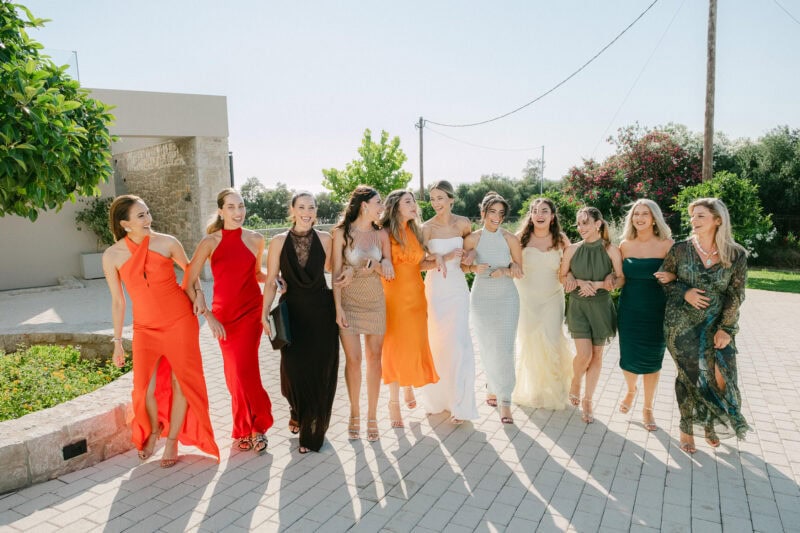 Bride and bridemaids in colorful dresses walking together outdoors on a sunny day.