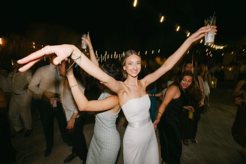 Young bride dancing at party with drinks in hand, smiling and enjoying the night.