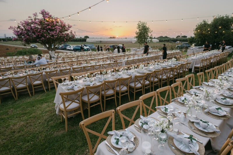 Outdoor wedding reception with long tables, string lights, and sunset view.