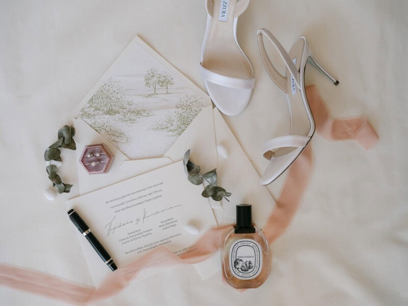 White high-heeled shoes with wedding invitation and perfume on satin fabric.