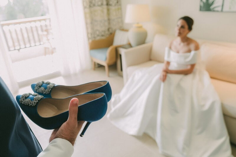 Blue bridal shoes in the foreground with the bride softly out of focus in the background