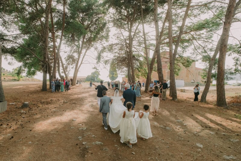 Bride walking with her family beneath the trees toward the wedding ceremony in Pylos