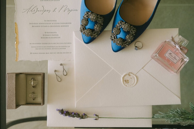 Blue bridal shoes, perfume, jewelry and wedding stationery arranged for a Costa Navarino wedding