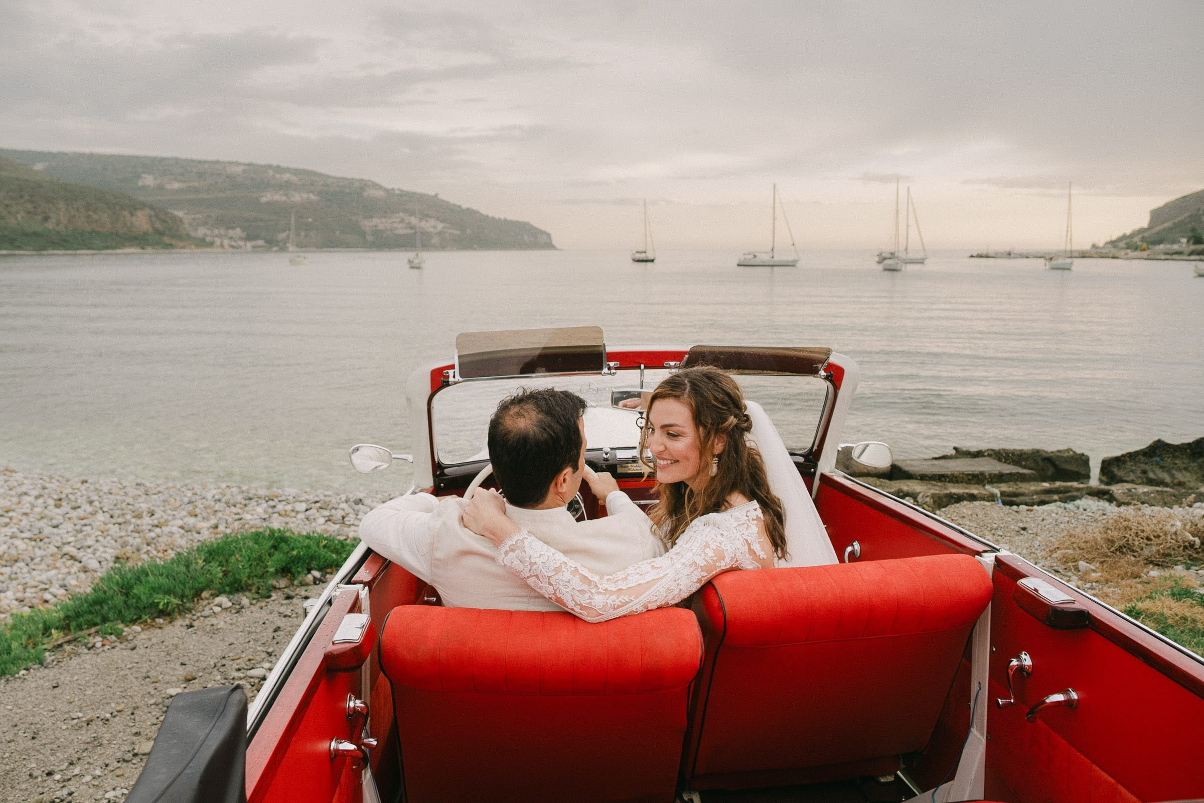Newlyweds embracing in a vintage car by the sea in Mani
