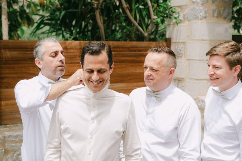 Groomsmen helping the groom prepare for his wedding in Mani