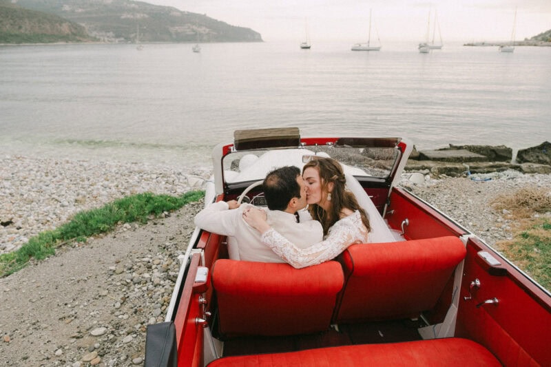Newlyweds embracing in a vintage car by the sea in Mani